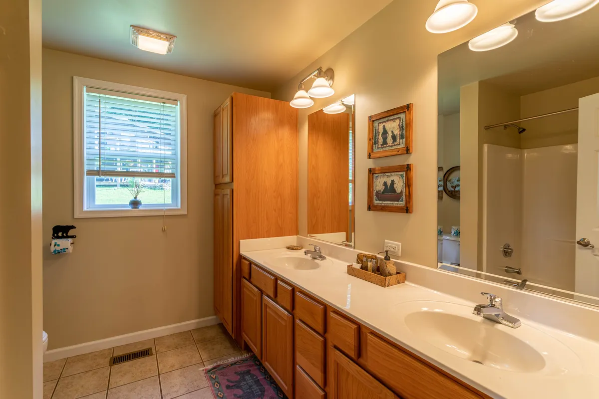 A spacious bathroom with a double vanity, large mirrors, and a window letting in natural light. The calm, organized space is suited for shared routines and family convenience.