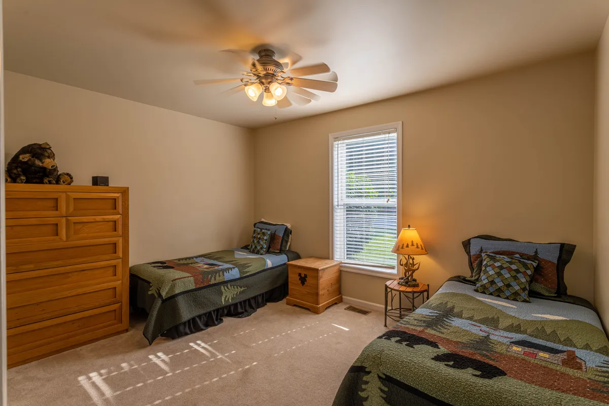 A cozy twin bedroom featuring two beds, a window overlooking the outdoors, a dresser, and a lamp. The space feels comfortable and relaxed, ideal for families or friends sharing a room.