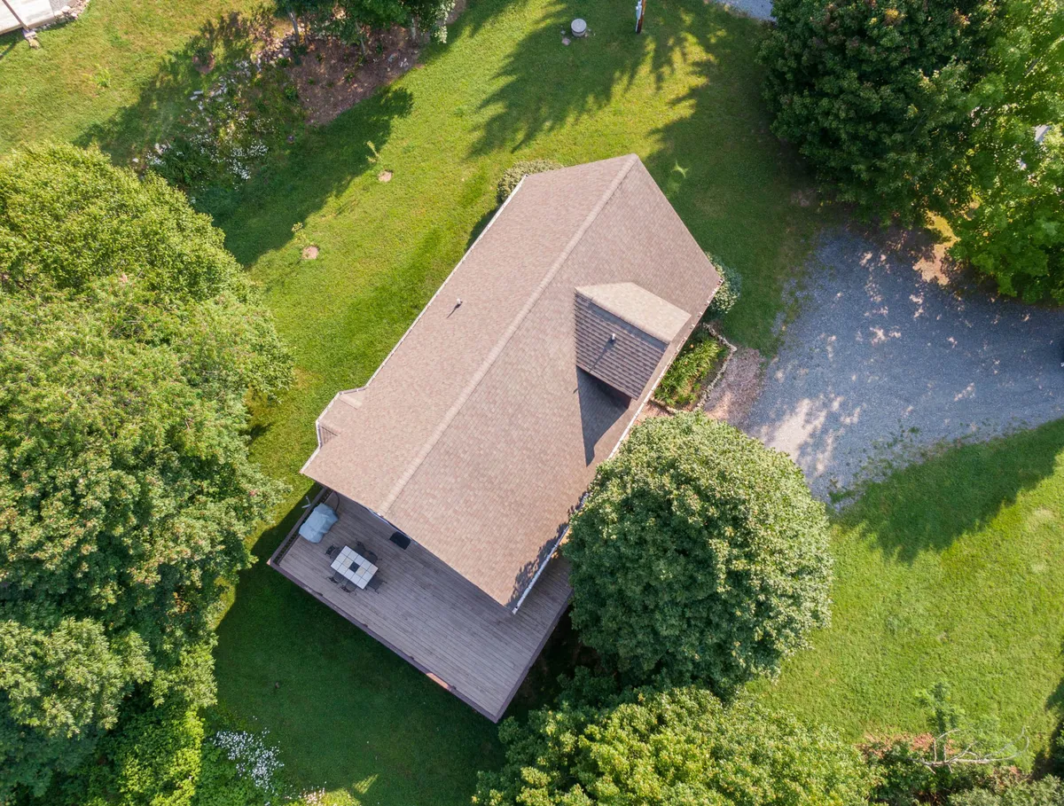 A peaceful exterior shot featuring the home’s deck area surrounded by trees and a gravel path. The deck is spacious, ideal for relaxing or outdoor dining, while the lush surroundings evoke privacy and connection to nature.