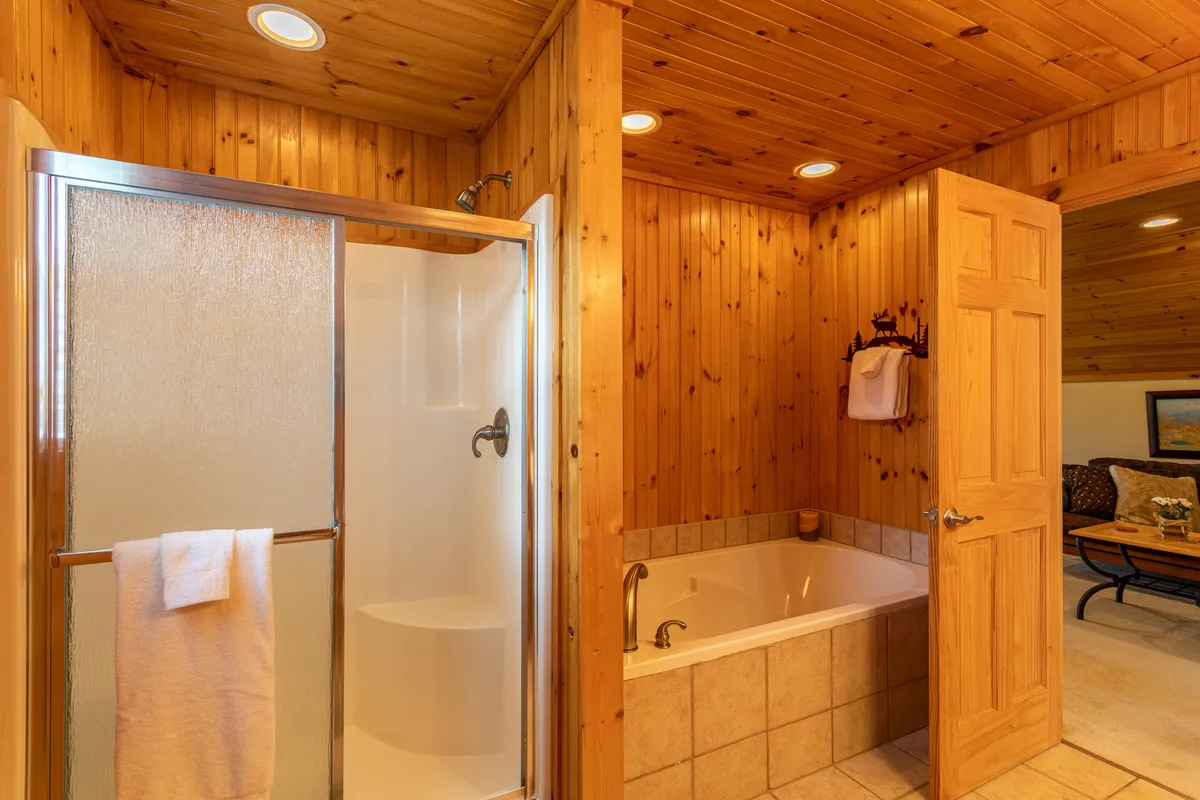 A tranquil bathroom scene with a soaking bathtub, modern shower enclosure, warm wooden wall paneling, and soft lighting. The space feels spa-like and inviting, ideal for unwinding after a busy day.