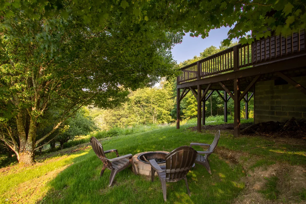 This scene focuses on the cozy fire pit area with wooden chairs arranged for gatherings, the edge of the deck visible nearby. The mood is serene, inviting guests to enjoy campfire nights, s’mores, and lively conversations under the stars.